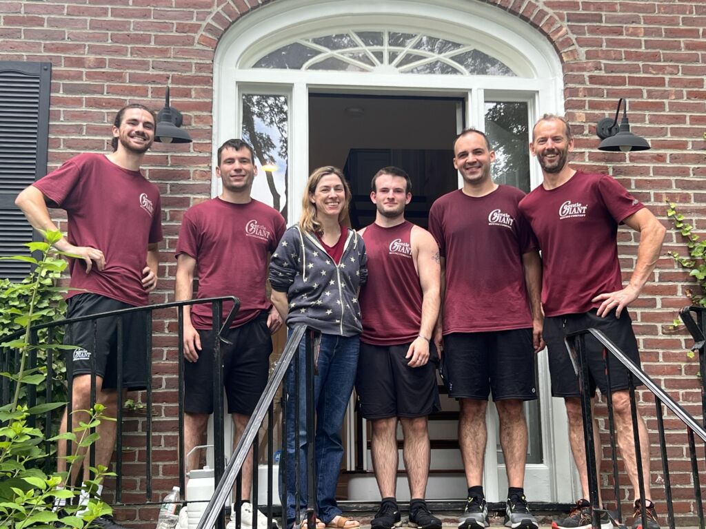 Five Gentle Giant movers are standing at the front door of a customer's home. The customer is standing with them.